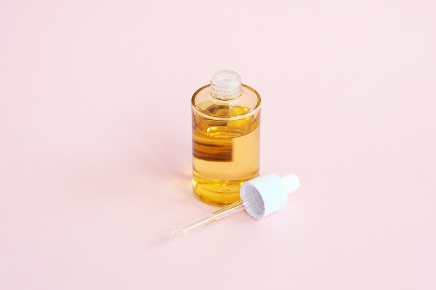 Amber facial oil with dropper on a soft pink background